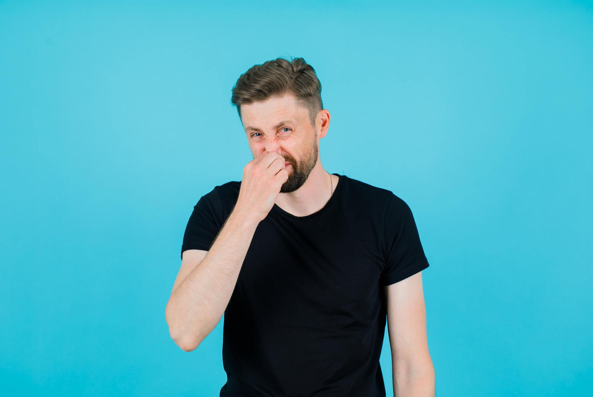 Young man holding nose with blue background